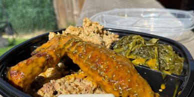 A delicious meal with glazed ribs, greens, and stuffing in a black container.