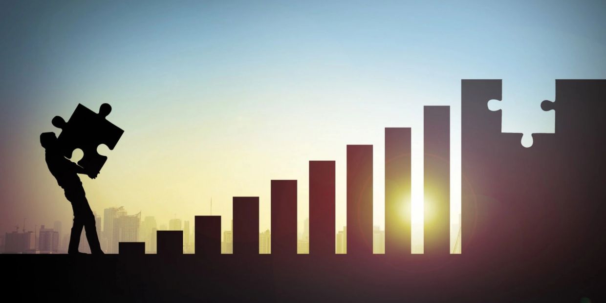 Silhouette of a person holding puzzle piece near rising bar chart.
