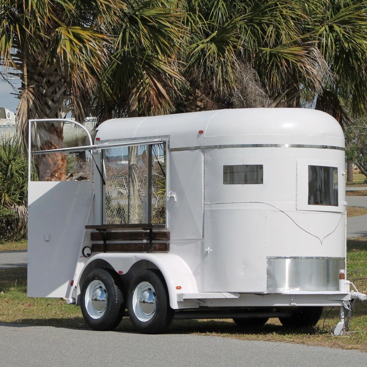 White horse trailer with open door parked near palm trees.