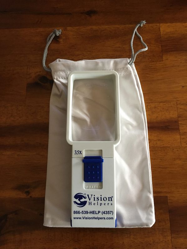 White handheld magnifier with 3.5X zoom on a white pouch on a wooden surface.