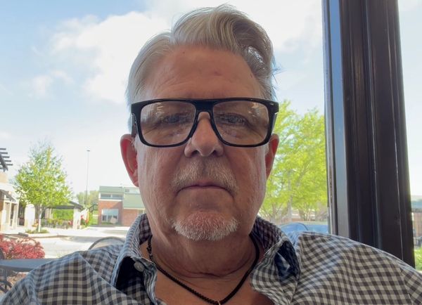 Older man with glasses and gray hair sitting indoors near a window.