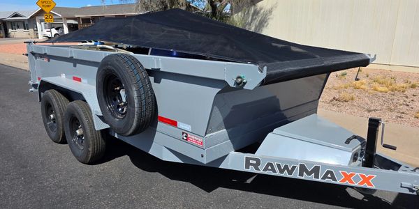Gray RawMaxx dump trailer with dual tires and a mesh cover parked on asphalt.