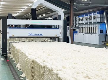 Industrial machine processing large cotton bales in a factory.