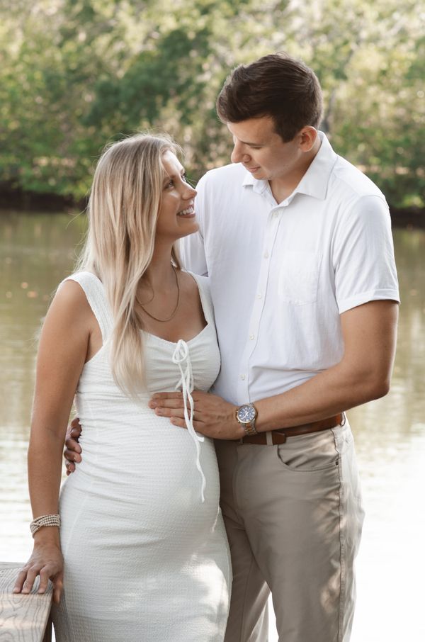 A couple smiles at each other while the husband holds the wife's pregnant belly 