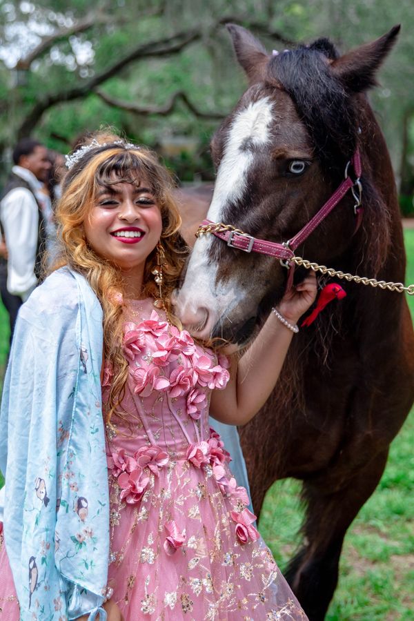 Smiling girl in quinceañera dress touches horses head