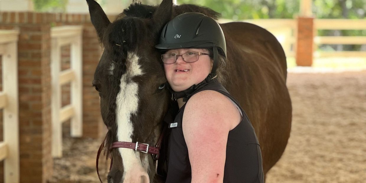 Adult woman with down syndrome smiling and hugging a brown horse