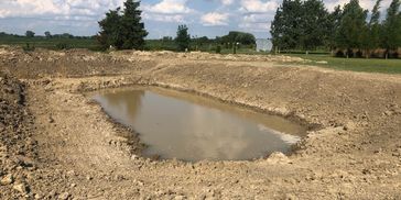 A newly dug pond filled with water in a rural area.