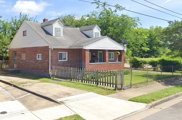 Small brick house with white trim and fenced yard on a sunny day.