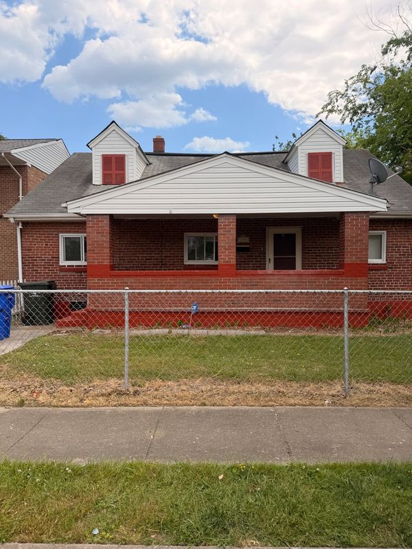 Brick house with red shutters and a chain-link fence in front.