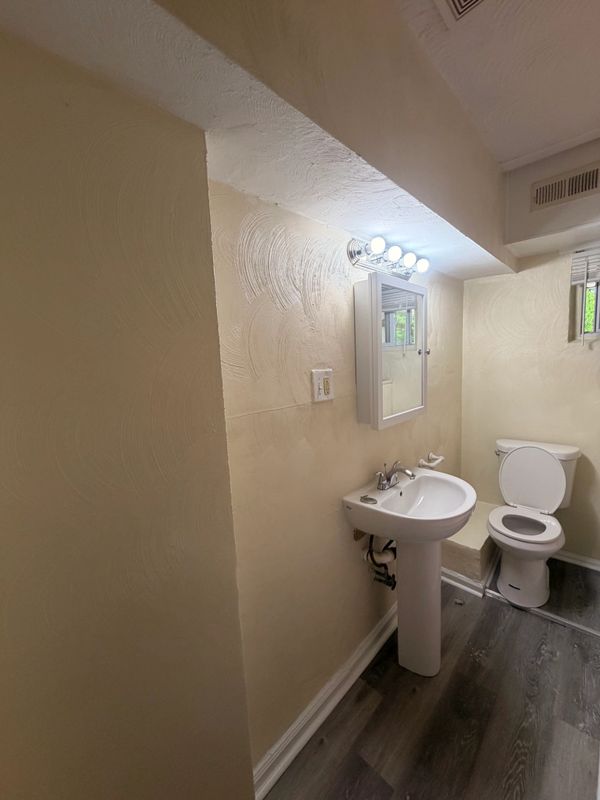 Small bathroom with pedestal sink, toilet, and overhead lights.