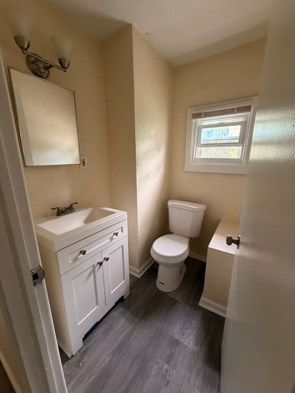 Small bathroom with white vanity, toilet, and window letting in natural light.