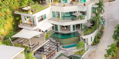 Modern white multi-level house with pool and greenery.