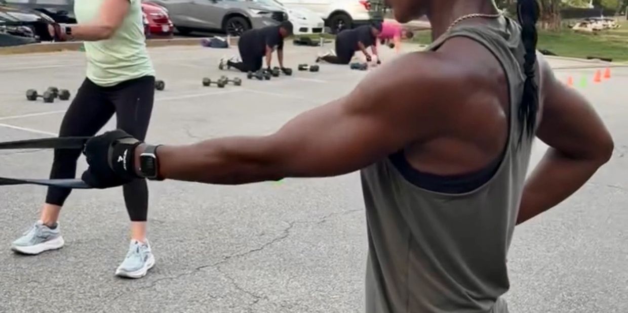People exercising outdoors using resistance bands and weights in a parking lot.