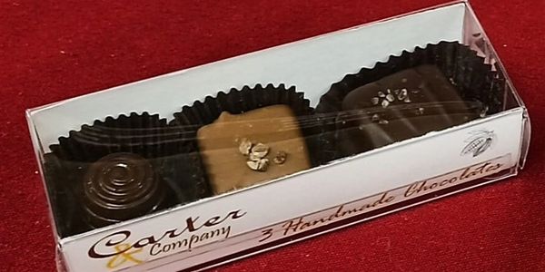 Box of three assorted handmade chocolates on red surface.