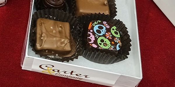 Box of assorted chocolates with colorful skull design on one piece.