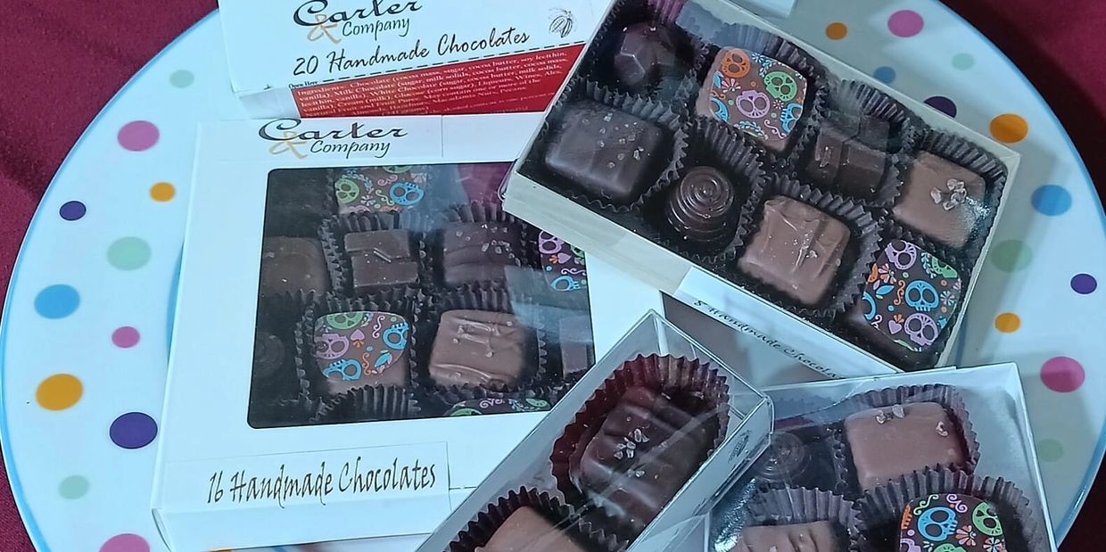 Boxes of handmade chocolates with colorful skull designs on a polka dot plate.