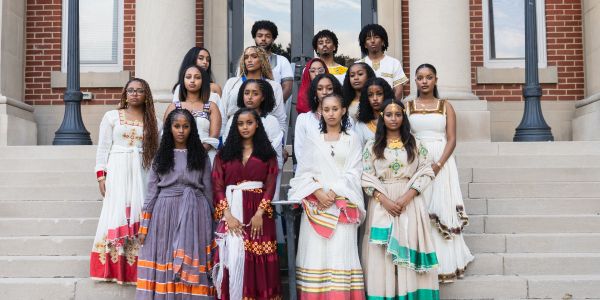 Group of young adults dressed in traditional attire posing on steps.