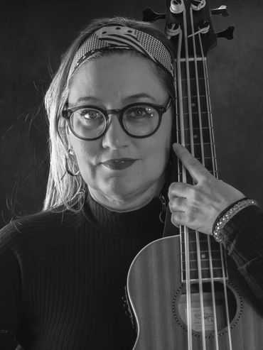 Woman with glasses holding an acoustic bass guitar, wearing a headband.