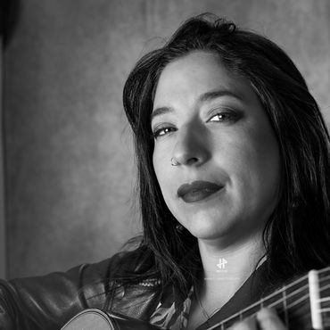 Black and white portrait of a woman holding a guitar, looking confidently at the camera.