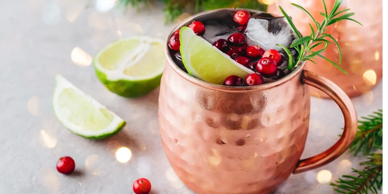 Festive cocktail in a copper mug with lime, cranberries, and rosemary.