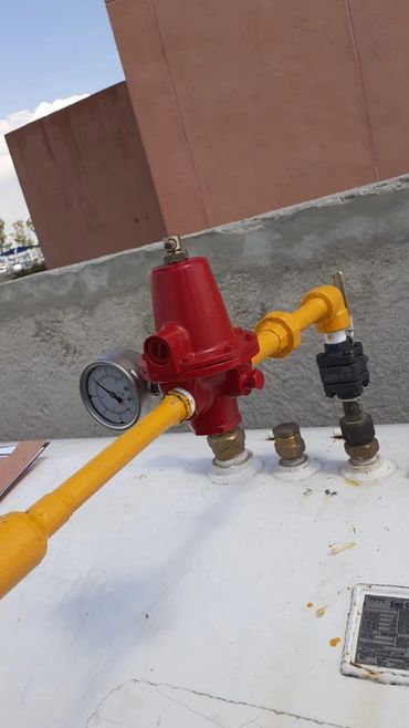 Red pressure regulator with yellow pipes on a white tank outdoors.