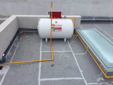 A white propane tank installed on a rooftop with yellow piping.