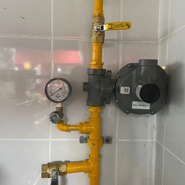 Yellow gas pipes with pressure gauge and valve attached on tiled wall.
