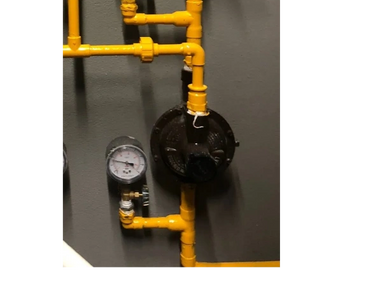 Yellow gas pipes with a pressure gauge and valve on a gray wall.