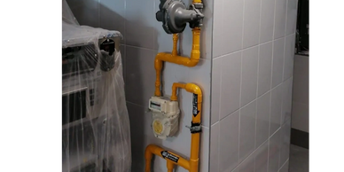 Yellow gas pipes installed along a tiled wall with a gas meter.