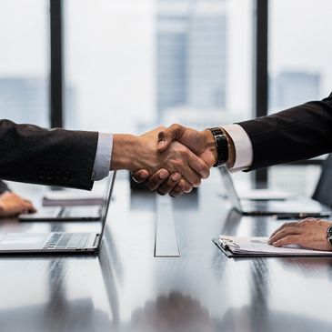 Two business professionals shaking hands over a conference table in an office.