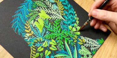 A hand painting vibrant green leaves on black paper.