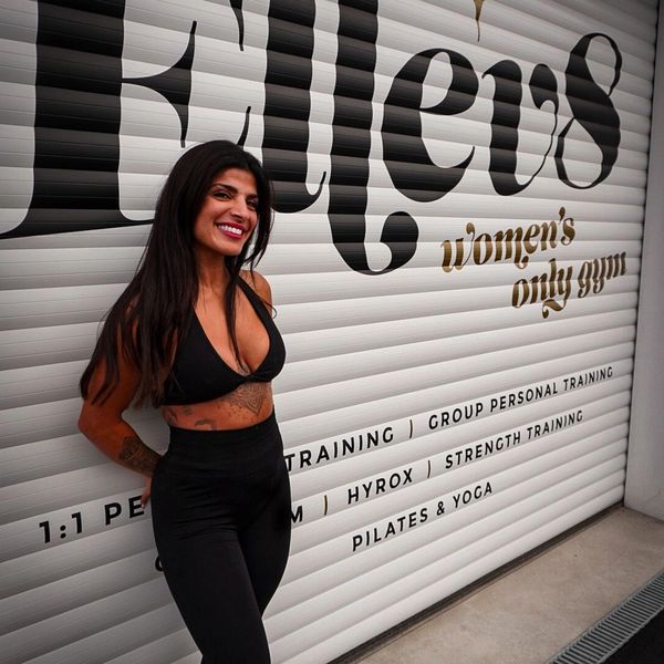 Woman in black workout attire smiling outside a women's only gym.
