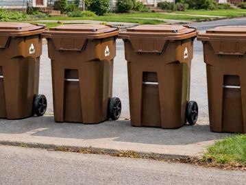 Four brown recycling bins lined up outdoors.