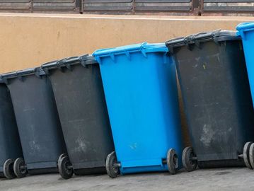 Row of black and blue wheelie bins lined up against a wall.