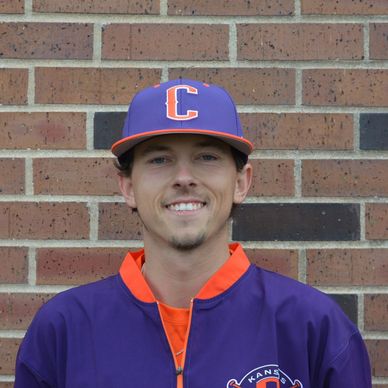 Young man in a purple baseball uniform smiling against a brick wall.