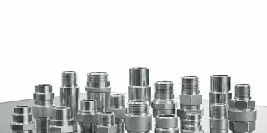Various metallic threaded pipe fittings arranged on a gray surface.