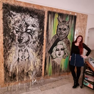 Woman standing next to two large, expressive paintings of dark, surreal faces.
