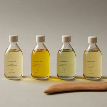 Four clear bottles of Aromatica skincare products arranged in a row with wooden spatulas.
