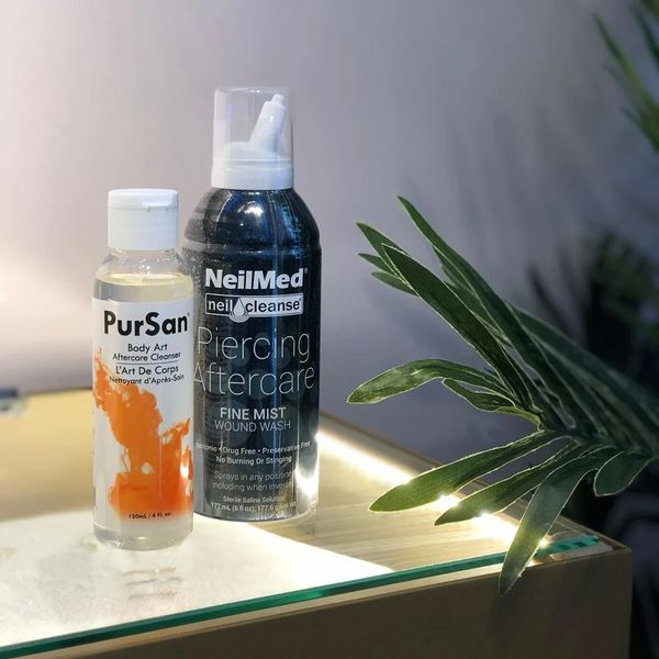 Two body art aftercare products on a glass surface with green plant beside them.