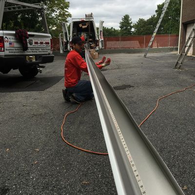 A technician from NJHMS prepares a seamless gutter for measuring its length for a precise cut.
