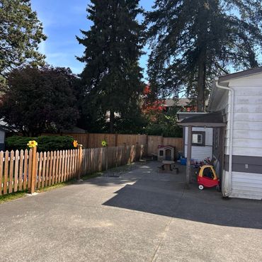 Sunny backyard with a wooden fence and children's playhouse and toy car.