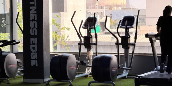 Modern gym equipment with elliptical machines and weights by a large window.