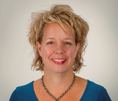 Smiling woman with curly blonde hair wearing a blue top.
