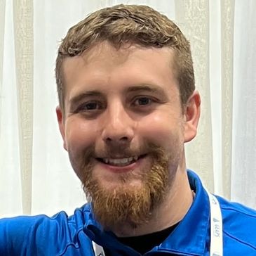 A smiling man with a beard wearing a blue shirt and lanyard.