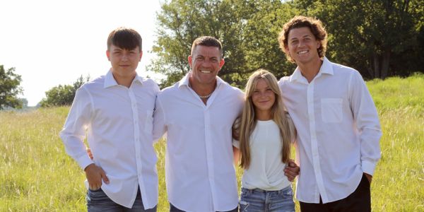 Family of four smiling outdoors in white shirts.