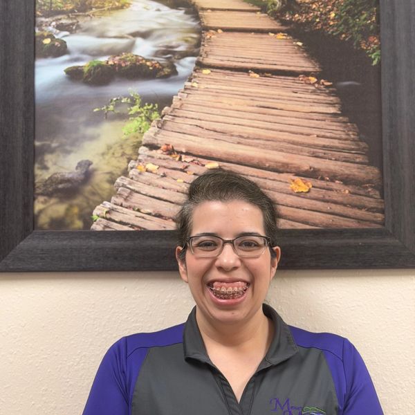 Smiling woman with braces in front of a framed wooden path photo.