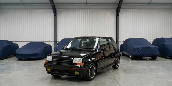 Black vintage car in a garage with covered vehicles.
