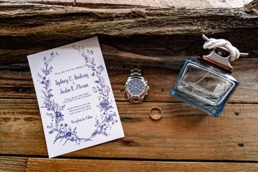 Wedding invitation, watch, ring, and cologne on rustic wood.
