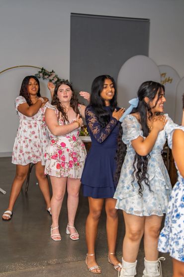 Four young women in floral and solid dresses dancing together indoors.