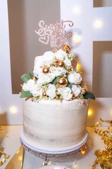 Elegant white cake decorated with white roses and gold ornaments.
